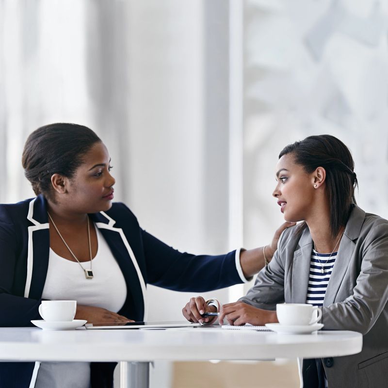 Shot of two coworkers talking together while sitting at a desk in an office
