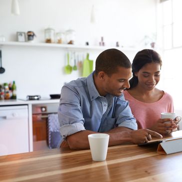 Couple enjoying coffee while using a tablet in a bright kitchen.
