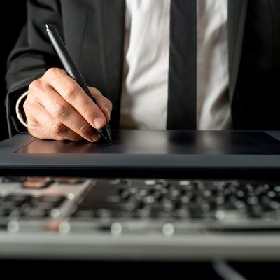 Businessman using a digital pen on a graphic tablet with a laptop keyboard in foreground.