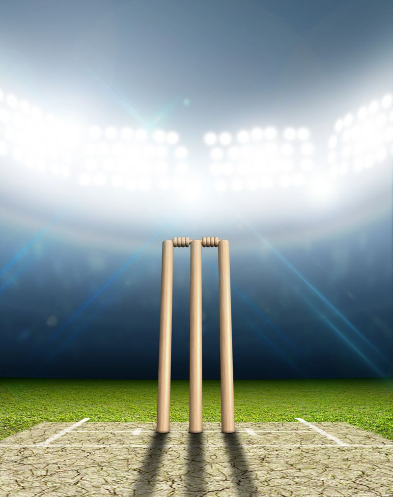 A cricket stadium with cricket pitch and set up wickets at night under illuminated floodlights