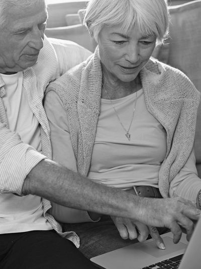 Elderly couple using a laptop together on a couch.