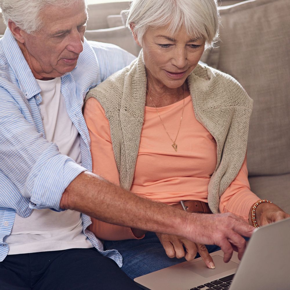 Elderly couple using a laptop together on the couch.