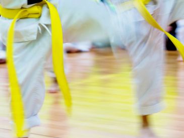 Two martial artists with yellow belts practicing kicks in motion.