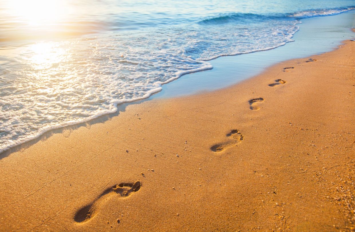 Footprints on a sandy beach near gentle ocean waves at sunrise.