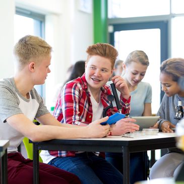 Teens collaborating in a science classroom, using microscopes and tablets.