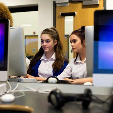 Two young women focused on working together at a computer in a classroom.