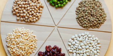 A wooden tray with six sections holding different types of dry legumes and peas.