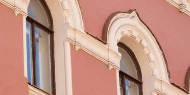 Two arched windows with white decorative trim on a pink building.