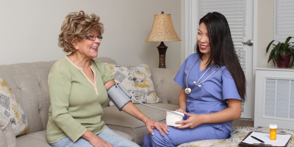 Nurse checking elderly woman's blood pressure at home.