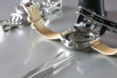 A wristwatch being repaired with precision tools on a reflective surface.