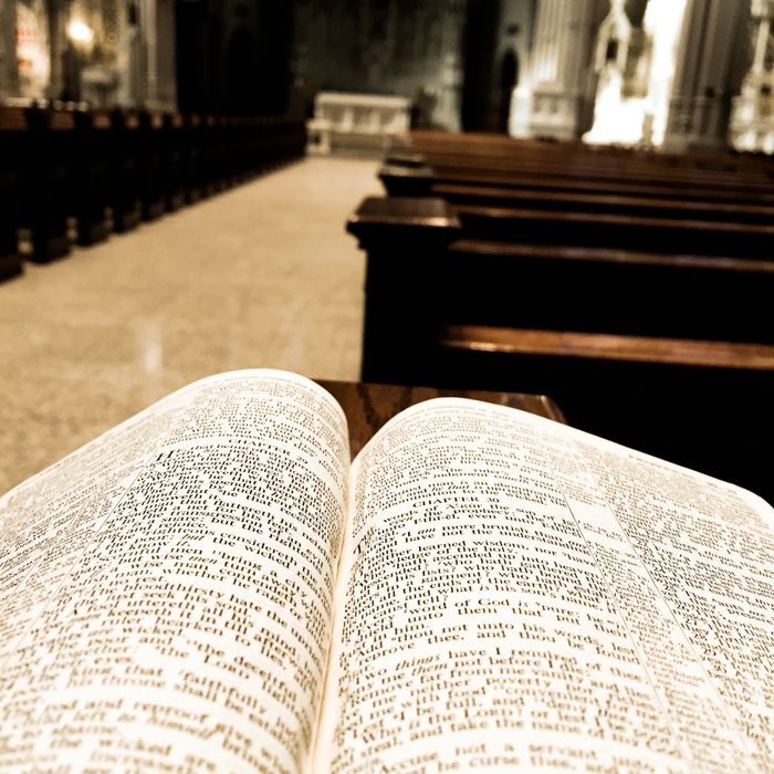 Open Bible on a church pew with empty rows leading to the altar.