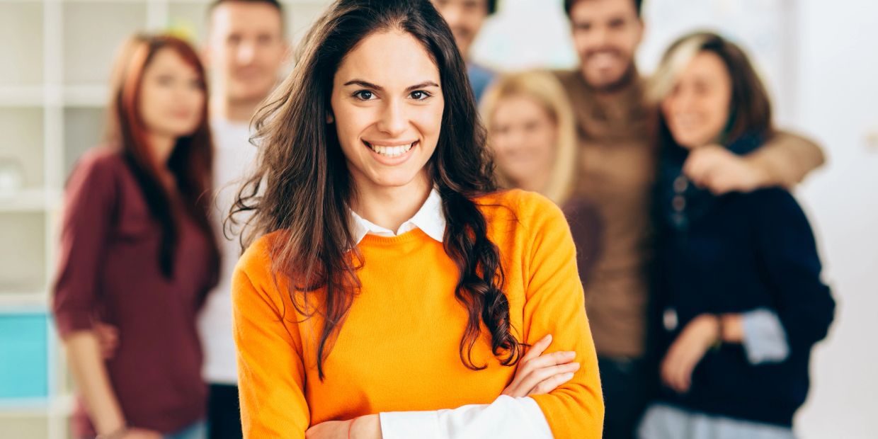 Confident woman in orange sweater with group behind her.