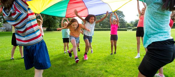 Kids playing with a colorful parachute outside.