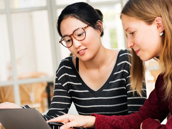 Two women collaborating while looking at a laptop screen.