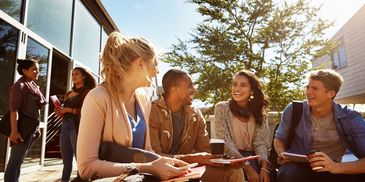 Group of diverse students chatting and smiling outdoors on a sunny day.