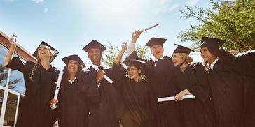 Group of happy graduates celebrating outdoors in caps and gowns.