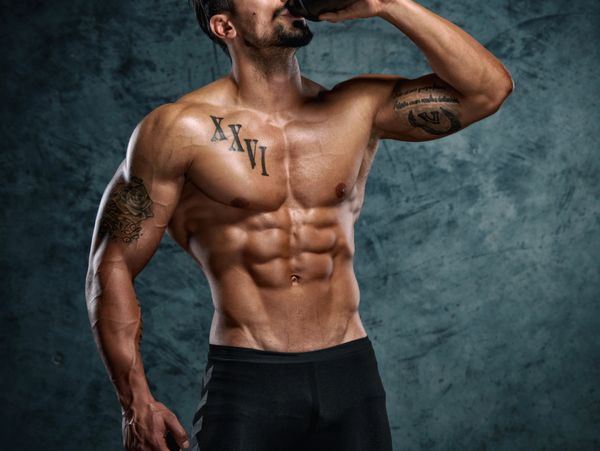 Muscular man drinking from a black bottle, showing defined abs and tattoos.