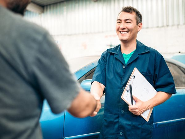 Mechanic shaking hands with a customer in a garage, holding a clipboard.