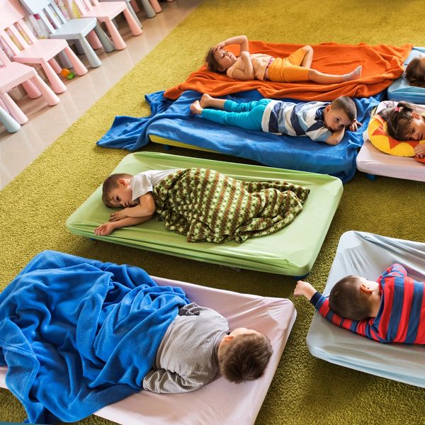 Children sleeping on mats with blankets in a daycare or preschool setting.