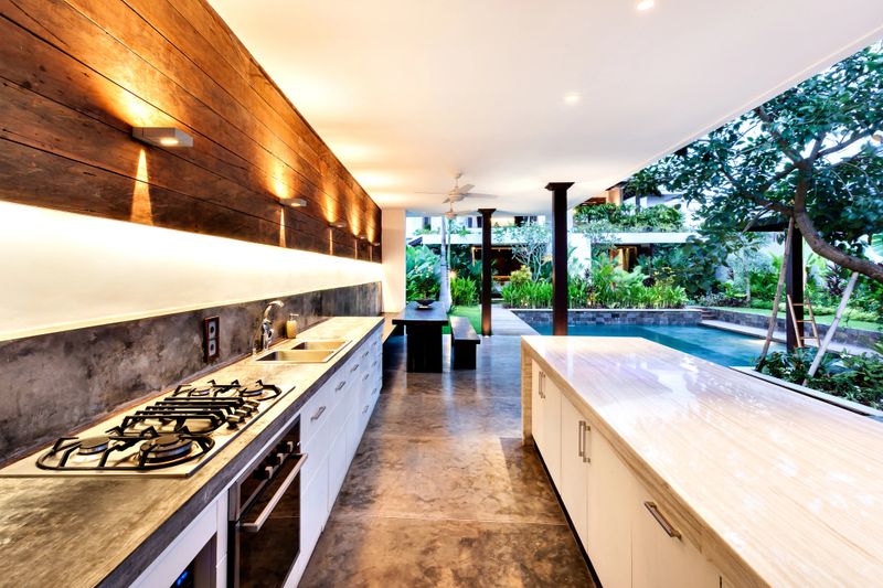 Outdoor kitchen with a stove an countertop next to garden including a pool in luxury hotel or house