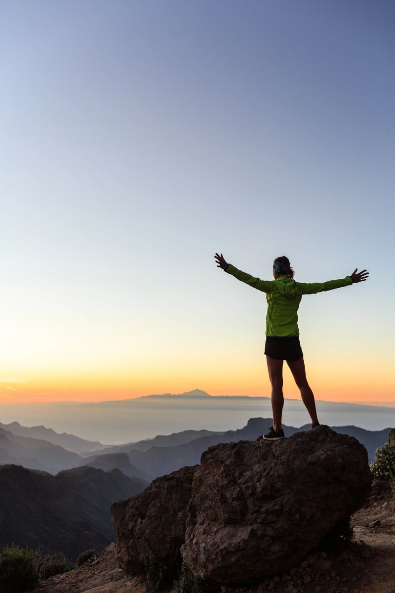 Woman successful hiking climbing silhouette in mountains, motivation and inspiration in beautiful sunset and ocean. Female hiker with arms up outstretched on mountain top looking at night sunset inspirational landscape.