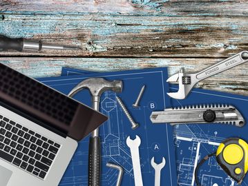 Tools and laptop on blueprints on wooden table.