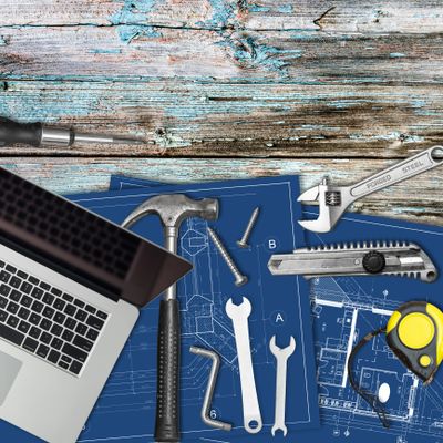 Laptop and tools arranged on blueprints on a rustic wooden surface.