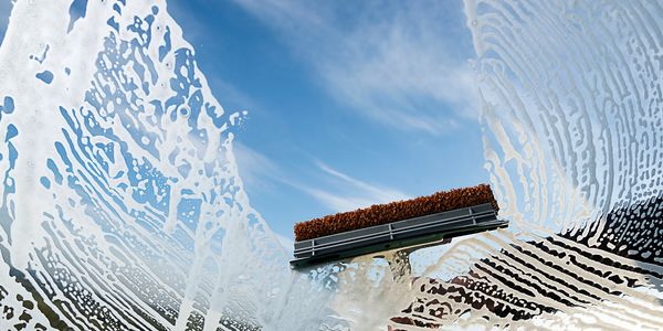 Cleaning a window with a soapy brush against a bright blue sky.