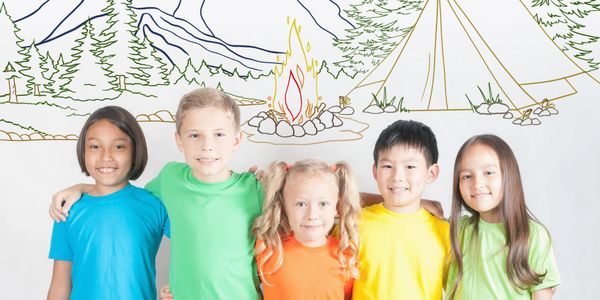 Five children in colorful shirts stand arm in arm in front of a camping mural.