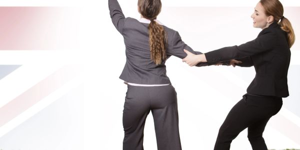 Two businesswomen in suits playfully pulling each other outdoors.