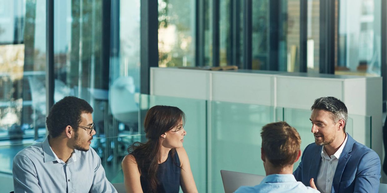 Four professionals engaged in a meeting around a white table in a modern office.