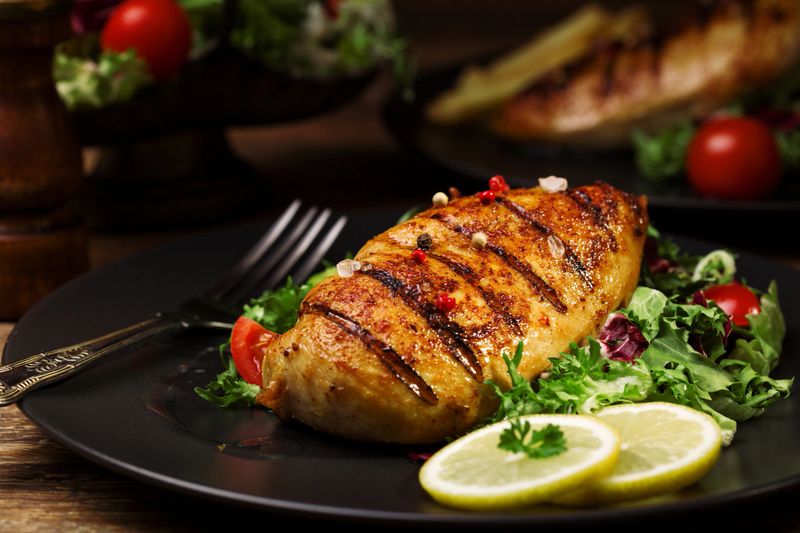 grilled chicken breast with green salad and french fries on a black plate.