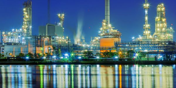 Illuminated industrial refinery at night reflecting on water.