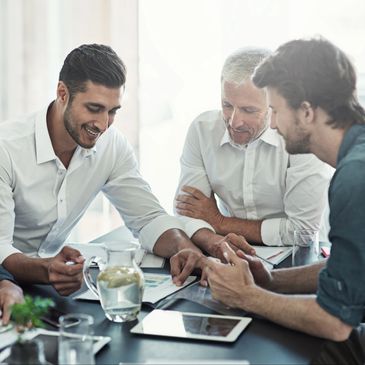 Three men discussing work around a table with documents and a tablet.