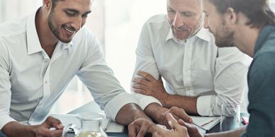 Three men discussing work around a table with documents and a tablet.