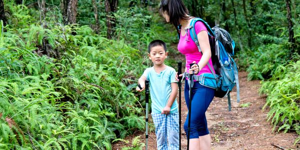 Mother and son hiking on a forest trail, surrounded by greenery.