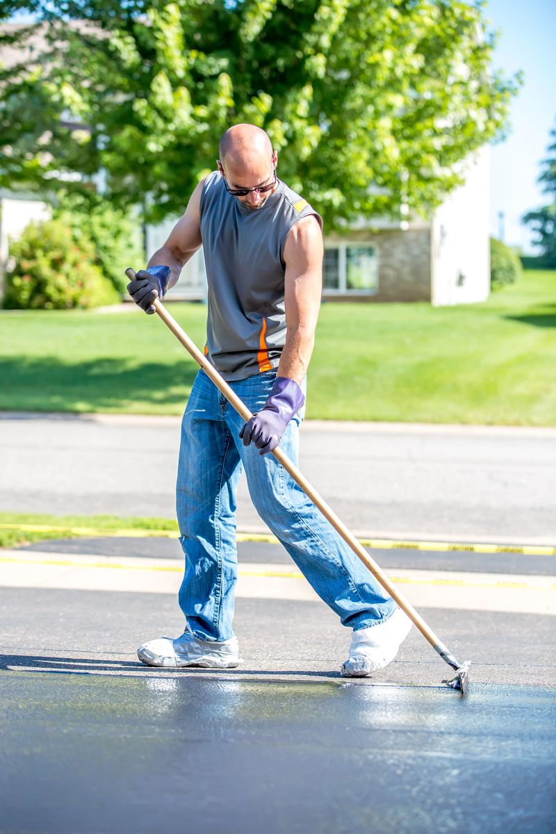 Close-up of a man seal coating his driveway as a do it yourself home improvement project. He is spreading the sealer on the driveway on a summer day.