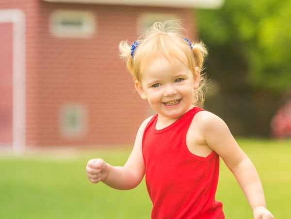 Smiling toddler in red tank top playing outdoors.