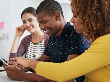 Three friends smiling and looking at a smartphone together.