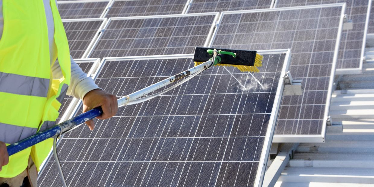 Worker cleaning solar panels with a brush and water.