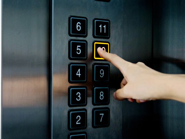 Hand pressing the 10th floor button in an elevator.
