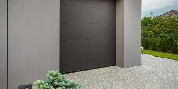 Modern garage with a sleek dark door and cobblestone driveway, accented by small tree and pathway lights.