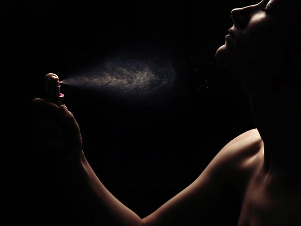 Person spraying perfume into the air in dim light.