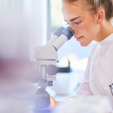 Mujer observando por un microscopio en un laboratorio.