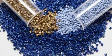 Colored plastic resin pellets in containers and scattered.