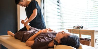 A woman receives a relaxing massage in a sunlit room from a male therapist.