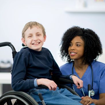 Smiling boy in wheelchair with a caring nurse beside him.