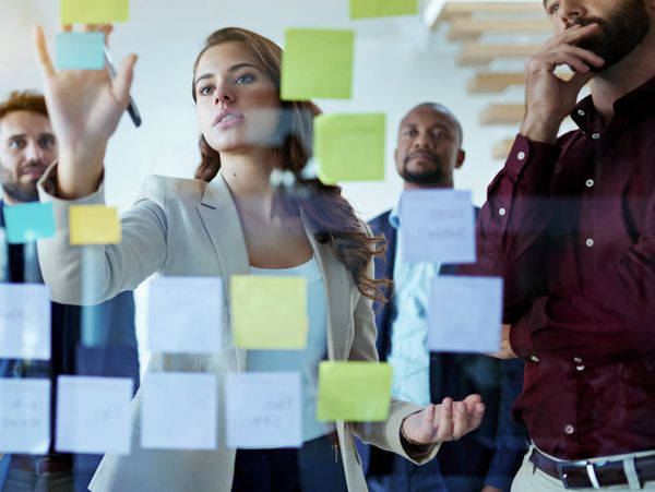 Team brainstorming ideas using sticky notes on glass wall.