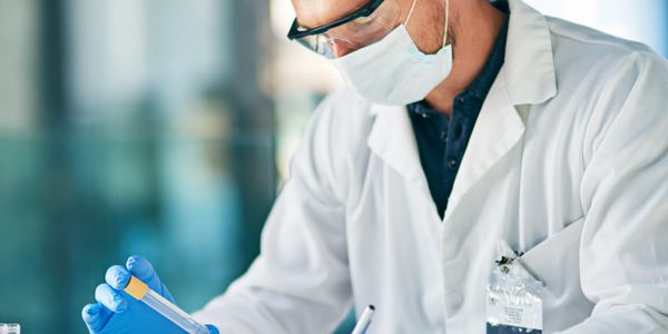 Scientist in lab coat examining a test tube and taking notes on a tablet.
