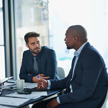 Two businessmen in suits having a serious discussion at a desk.